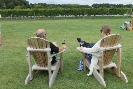 2 people savoring a glass of wine in chairs by the vineyard
